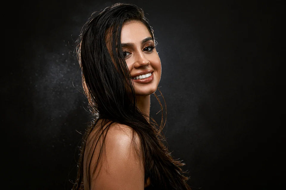 Uśmiechnięty portret beauty z mokrymi włosami na ciemnym tle