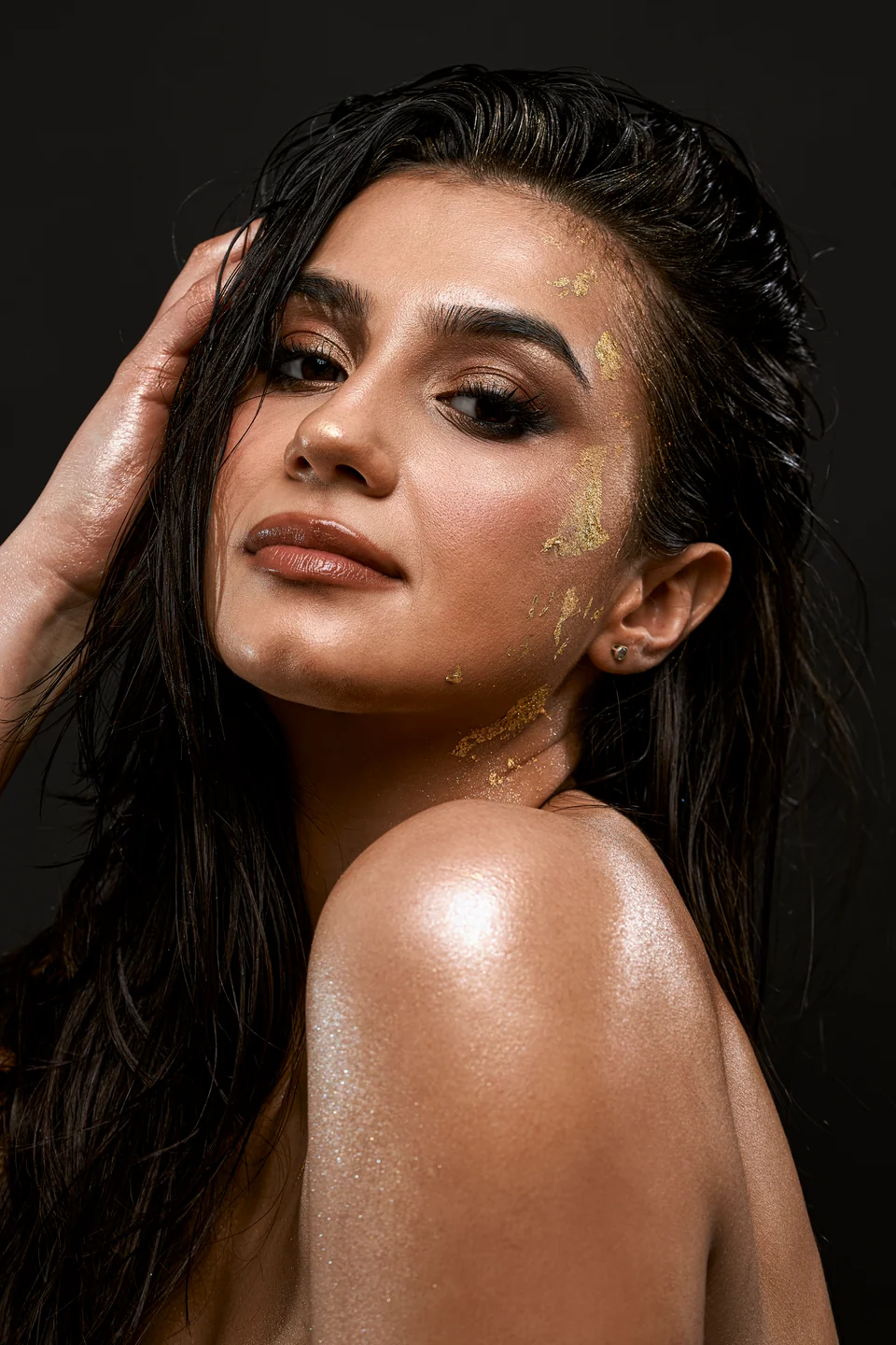 Portret beauty z płatkami złota i dłonią w mokrych włosach