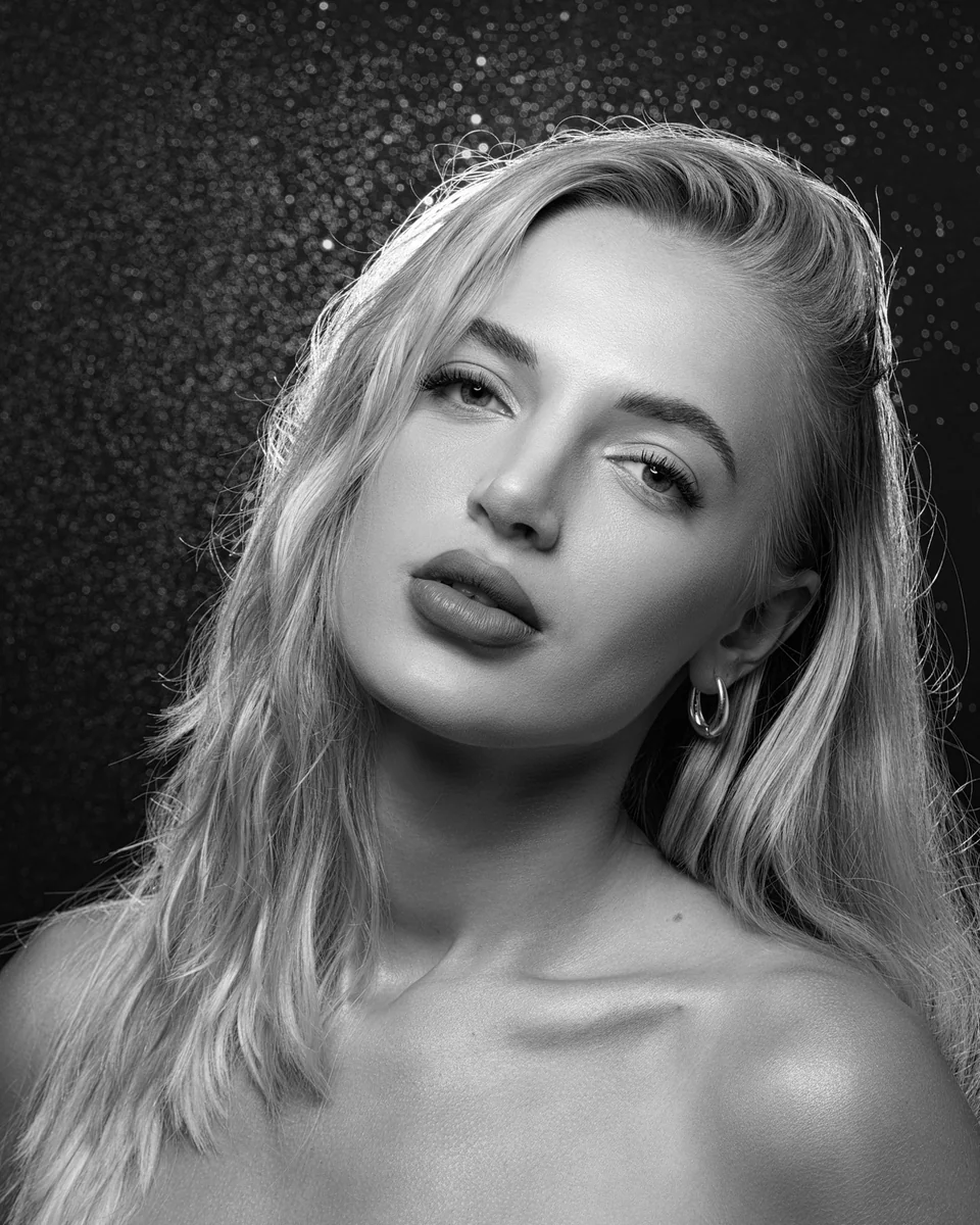 Czarno-biały portret beauty blondynki z bliska, z kolczykami kołami na ciemnym, połyskującym tle
